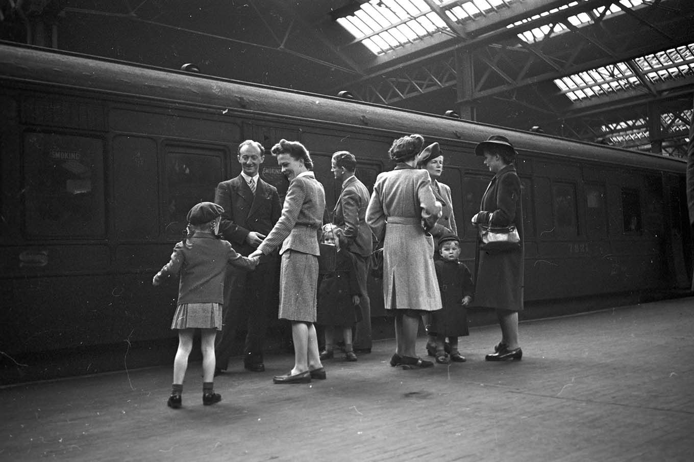 En gruppe mennesker ved siden av et tog, på en innendørs jernbanestasjon. Foto.