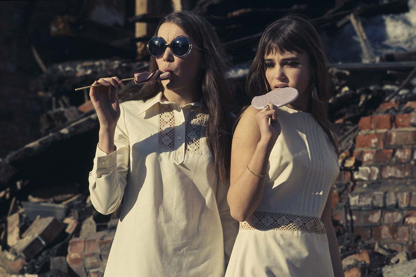 To kvinner i hvite kjoler med kjærlighet på pinne, stående på en nedrivningstomt. Foto.