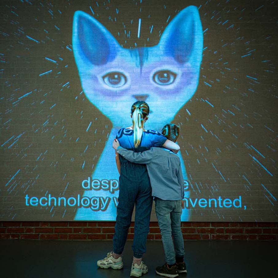 En ung jente prøver Virtual reality. To unge gutter står og ser på. Foto