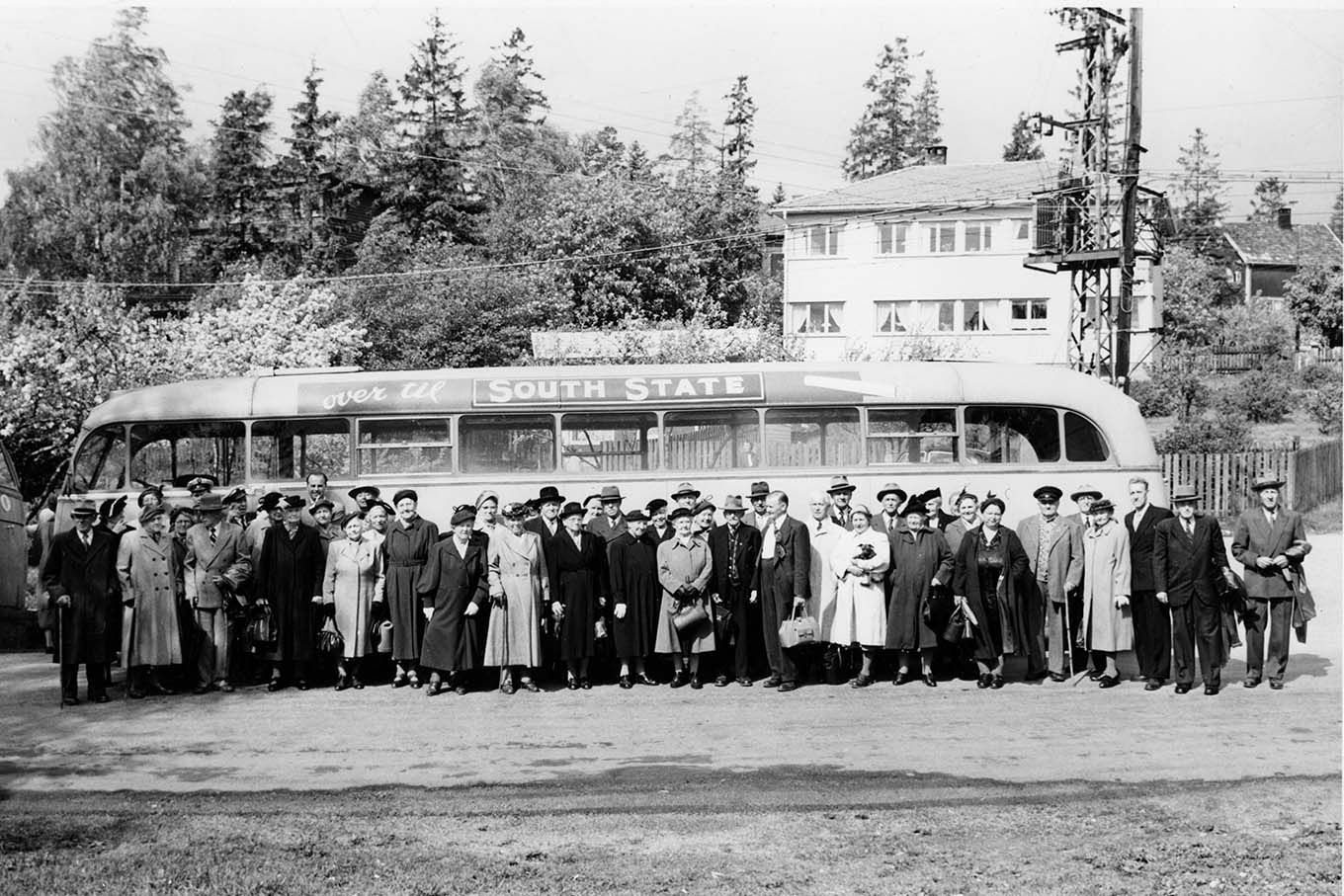 En gruppe eldre personer foran en buss. Korsvoll, Oslo, 1956. Foto.