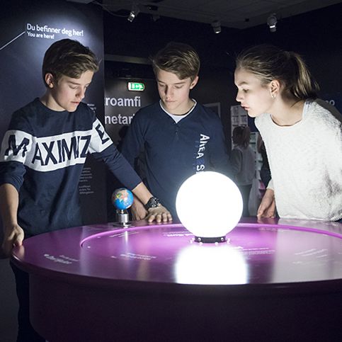 Tre ungdommer står og ser på en modell av et solsystem. Foto.