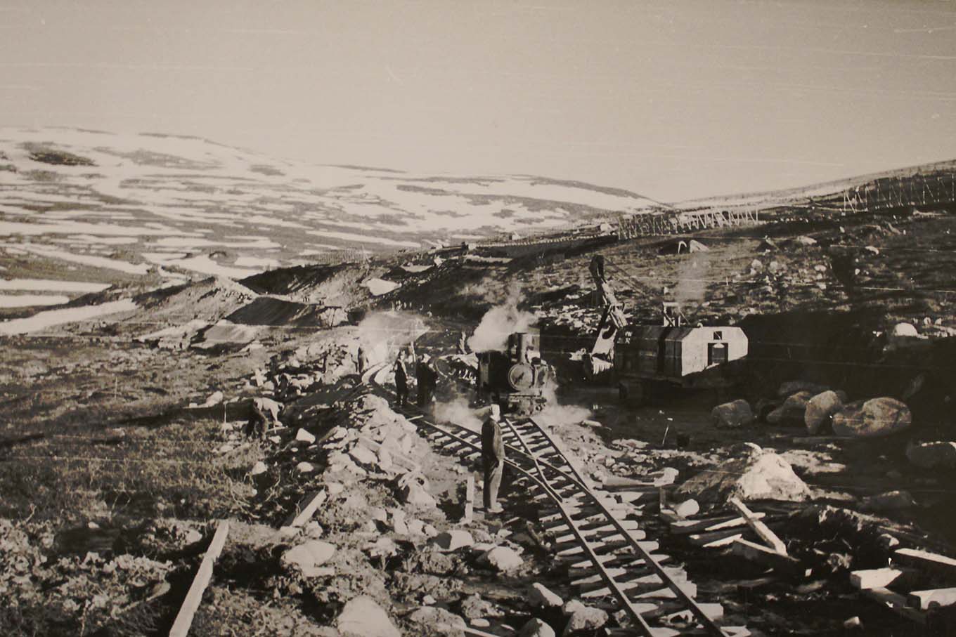 Tvangsarbeidere ved et jernbanespor over fjellet, et lokomotiv ankommer. Foto.
