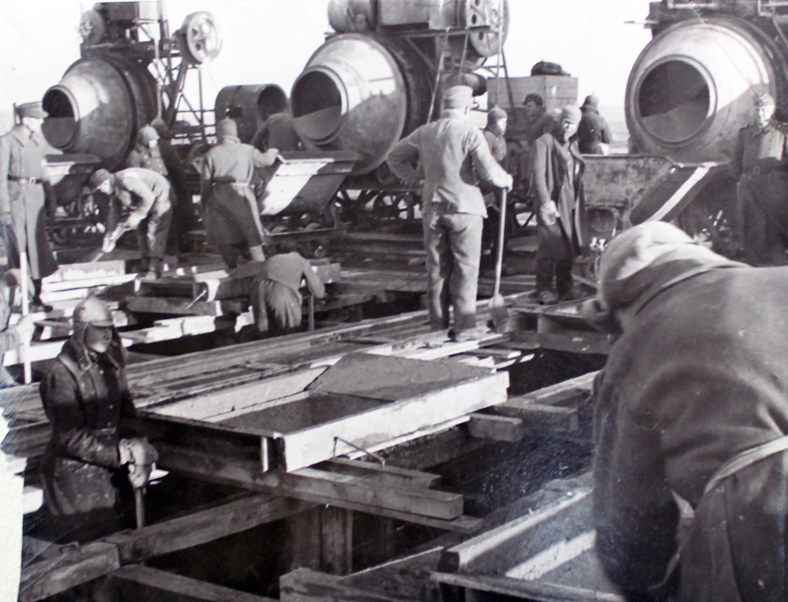 Tvangsarbeidere og militærvakter ved sementblandere og trekonstruksjoner. Foto.