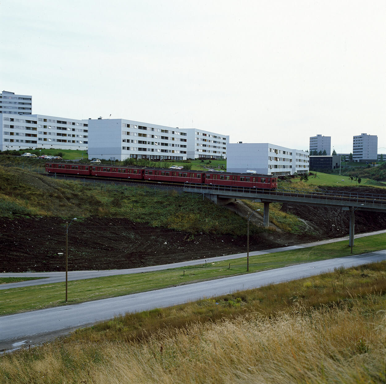 t-bane kjører forbi blokker på stovner i grønn natur 