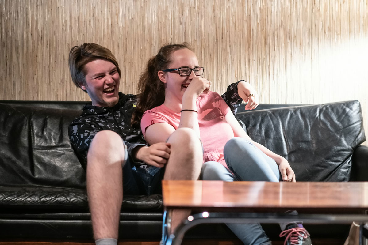 To ungdommer ler seg i hjel mens de sitter i en sofa. Foto.