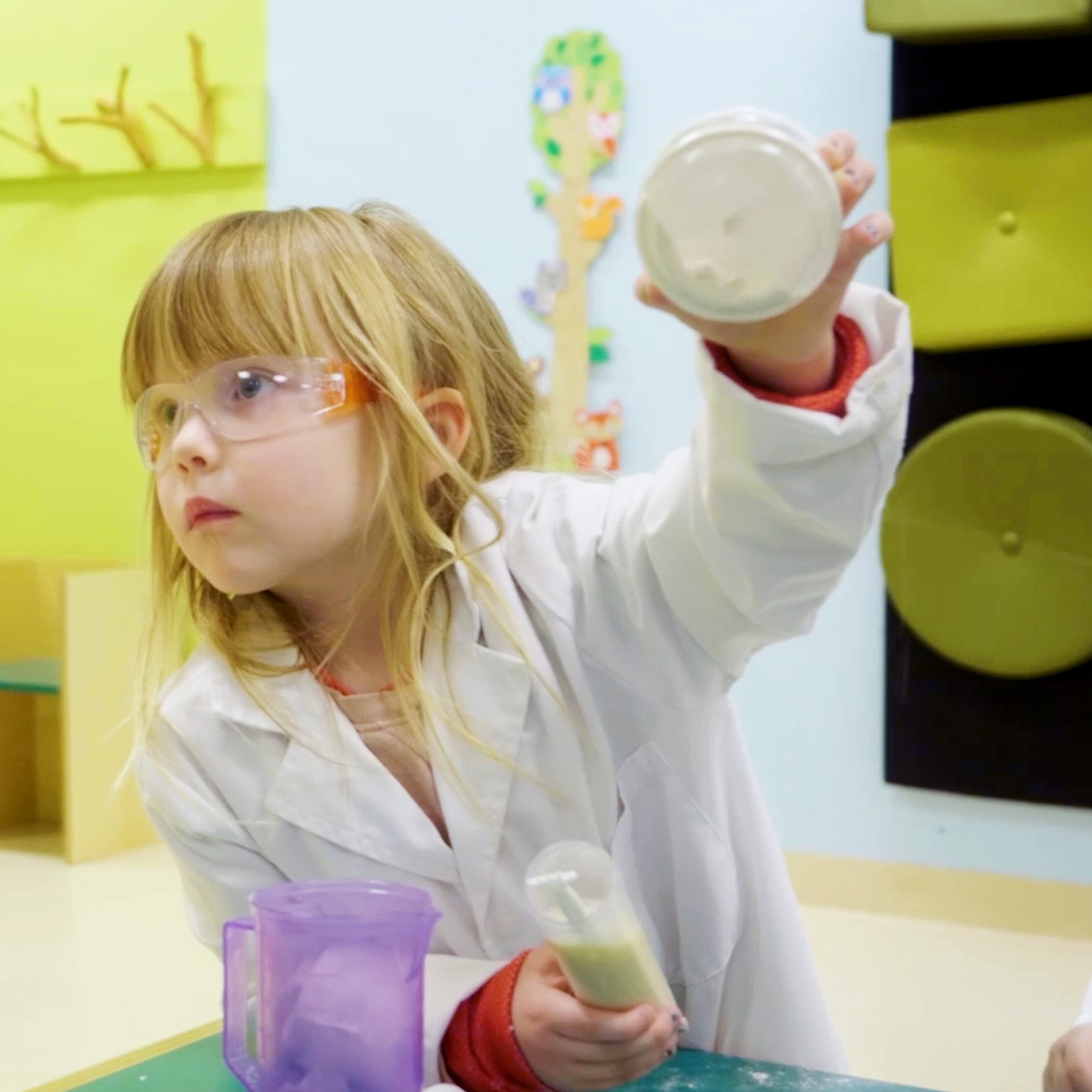 En jente i labfrakk rekker opp hånden. Foto. 