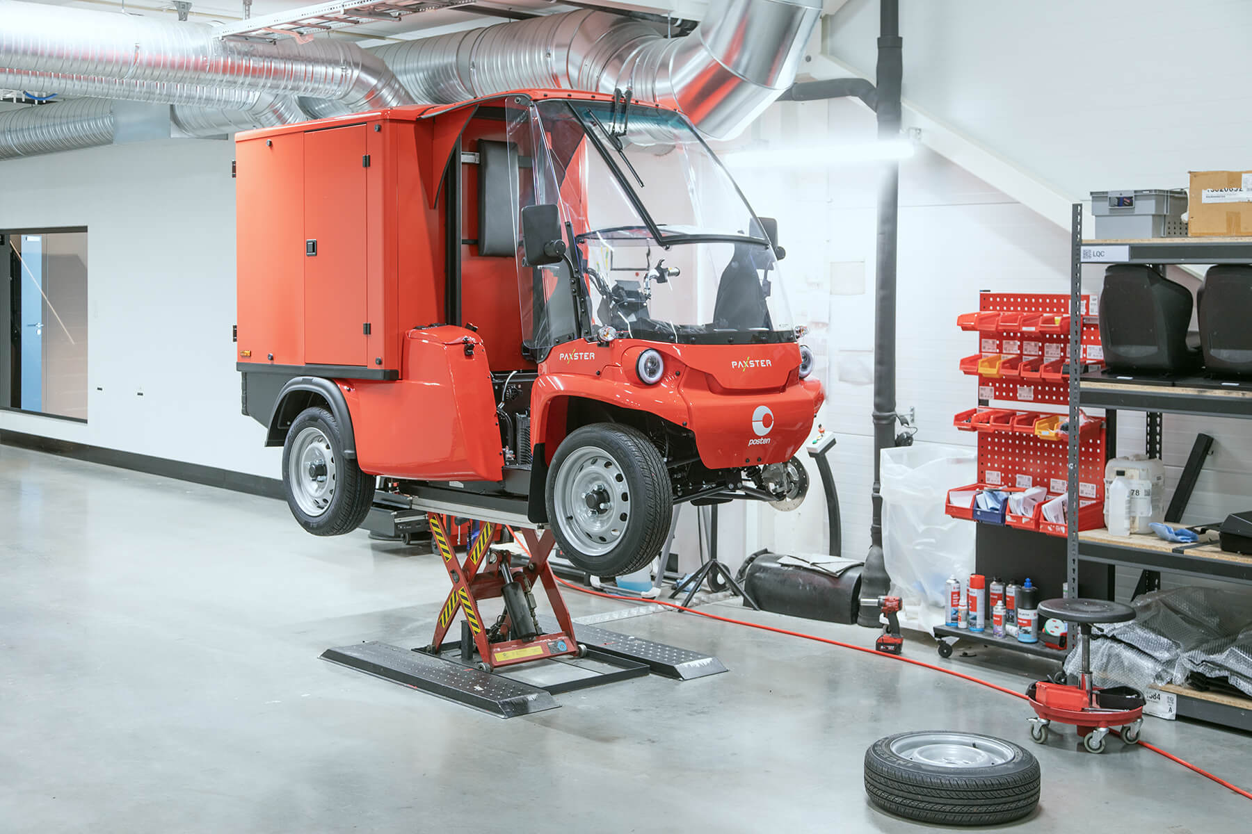 Rød Paxster postbil under produksjon i fabrikk med verktøy
