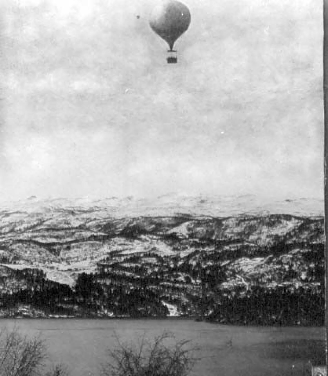 Gammel illustrasjon av en luftballong som svever høyt over et fjellandskap.