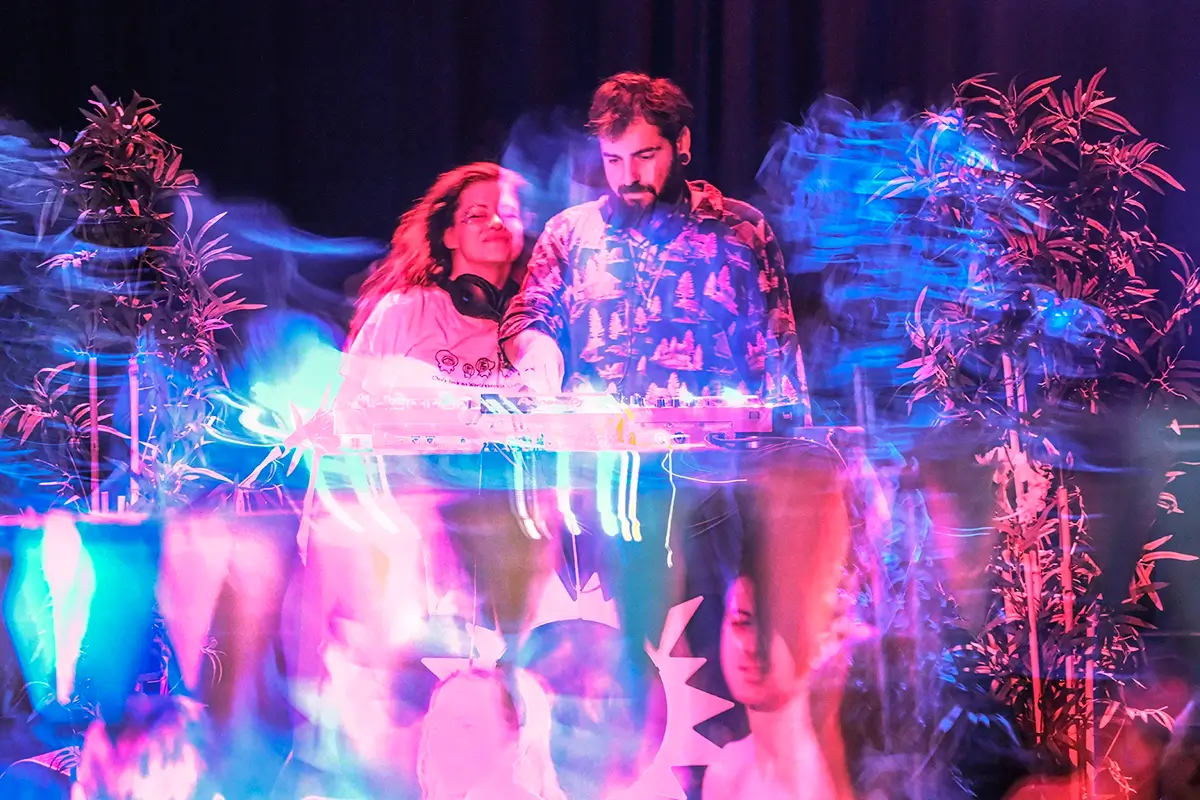 mannlig og kvinnelig DJ i neon farger foran et dansegulv med mennesker