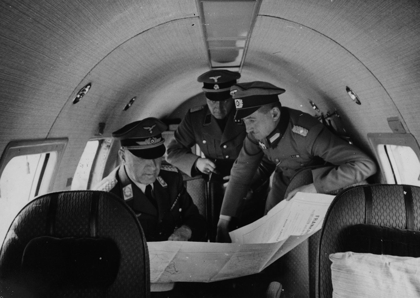 Uniformed men study a map aboard a plane. Photo. 