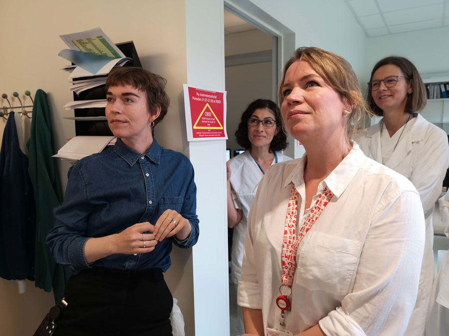 Fire kvinner står og ser på noe. To av dem har på seg lege klær.