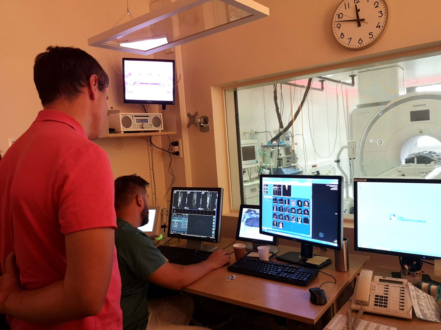 To menn står ved flere dataskjermer og kontrollerer en stor medisinsk skanner.