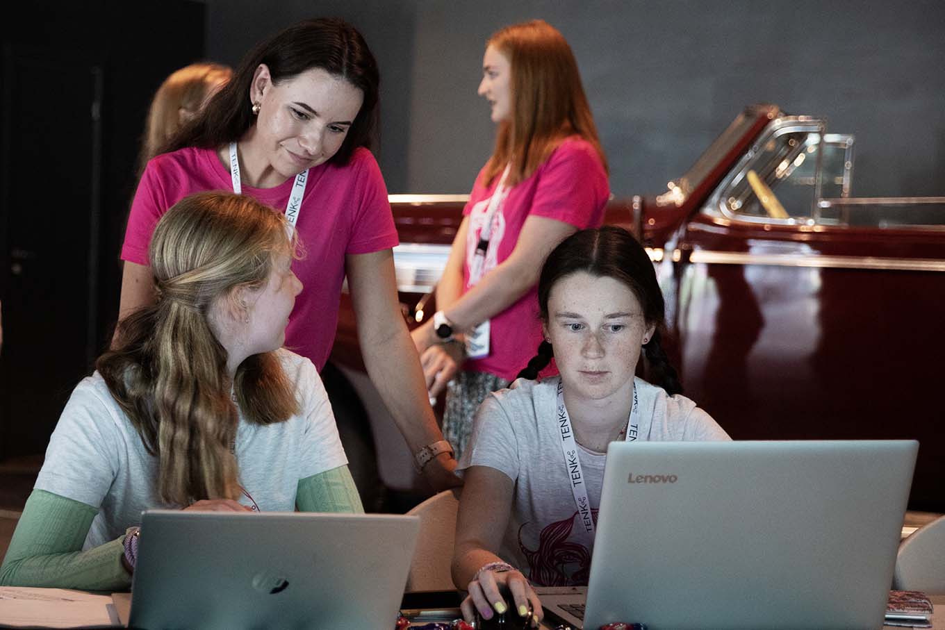 Two girls in front of a computer talking to a female supervisor. Photo.