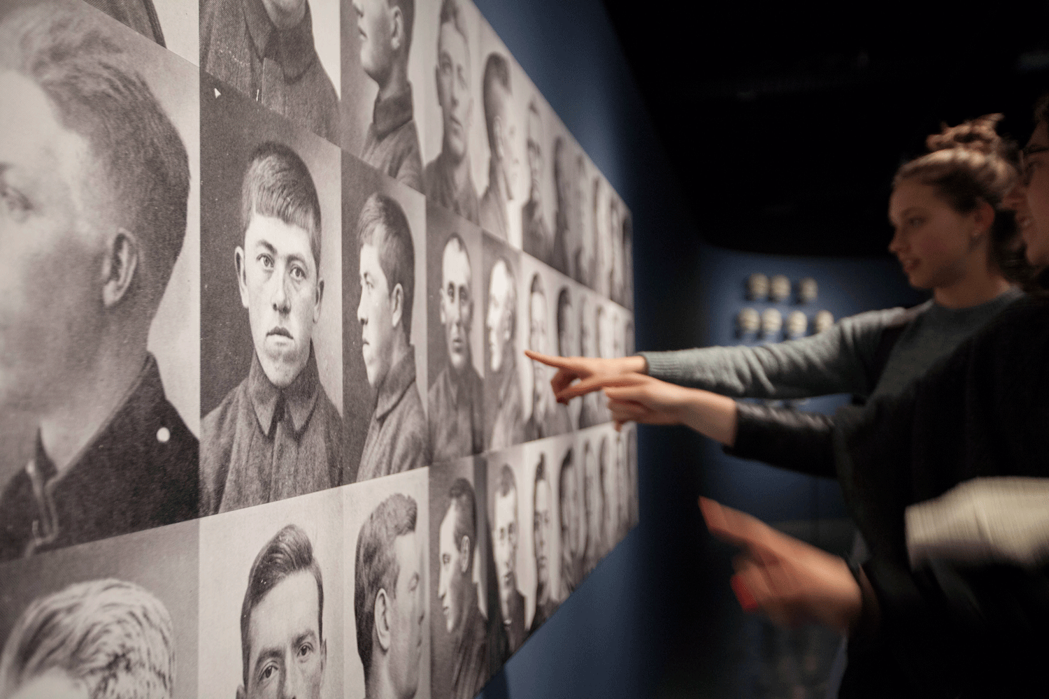 Personer som peker på en rekke med svart-hvitt portretter i en utstilling