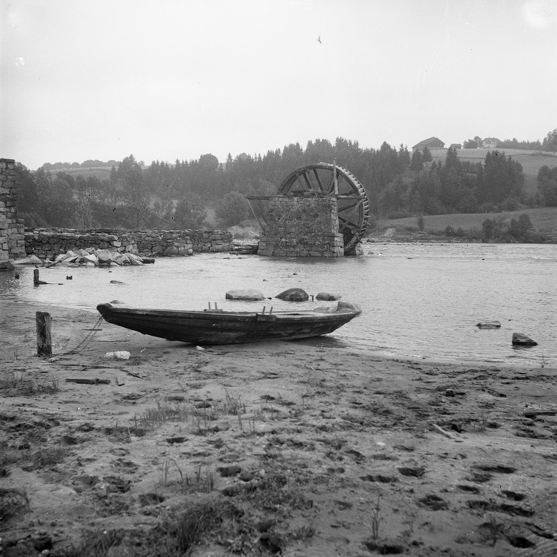 Pram ved elvebredden med vannhjulet i bakgrunn 