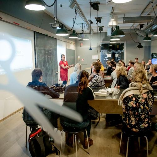 To kvinner som syr metalltråd i tekstil i et undervisningsrom. Foto