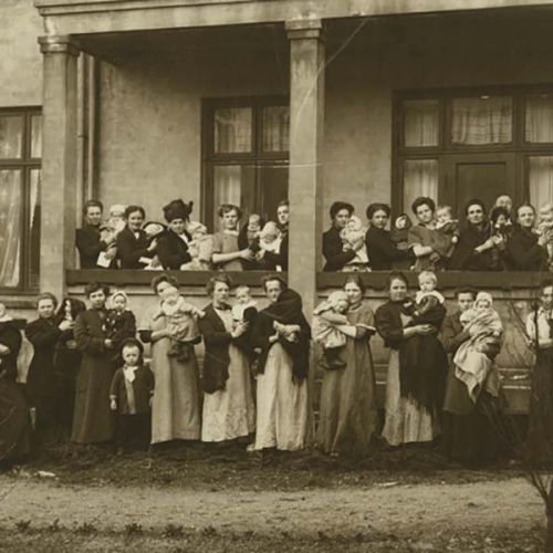 Several women stand in front of a house with a child in their arms. Photo.