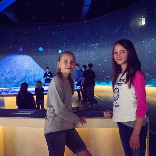 Two girls stand in front of a screen. Photo.