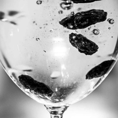 Rosiner i et vinglass med karbonisert vann. Foto