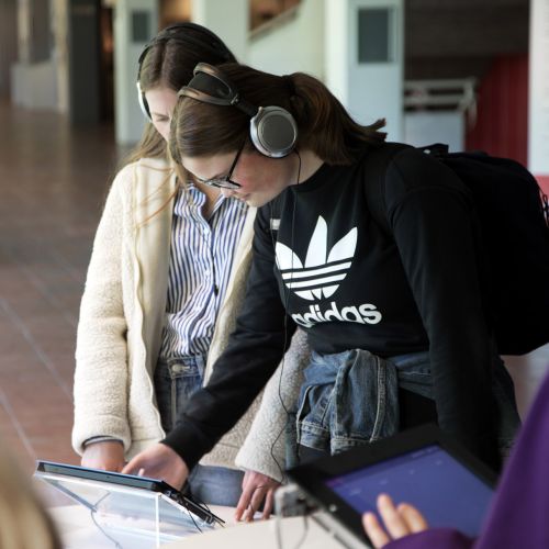 Two girls are looking at an iPad and wearing headphones. Photo.