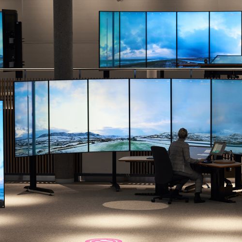 Kvinne i kontrolltårn foran store skjermer
