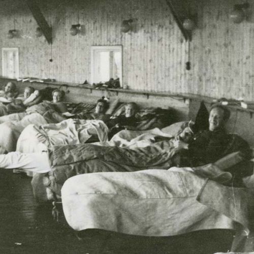 Several people are lying in beds that are lined up along a row. Photo.