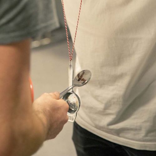 En gutt slår en skje mot en annen skje som er festet i en snor. Foto