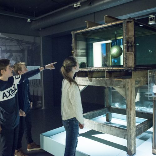 3 young people stand around the scientific instrument Terrella. Photo
