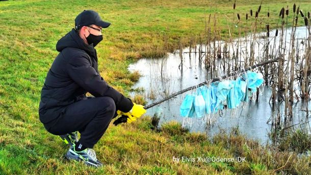 Man fishes out a face mask from a pond. Photo.