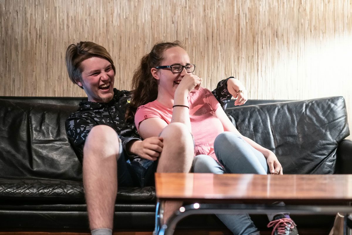 To ungdommer ler seg i hjel mens de sitter i en sofa. Foto.