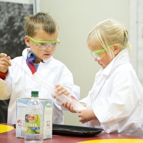 Two children wearing protective gear doing a chemistry experiment. Photo.