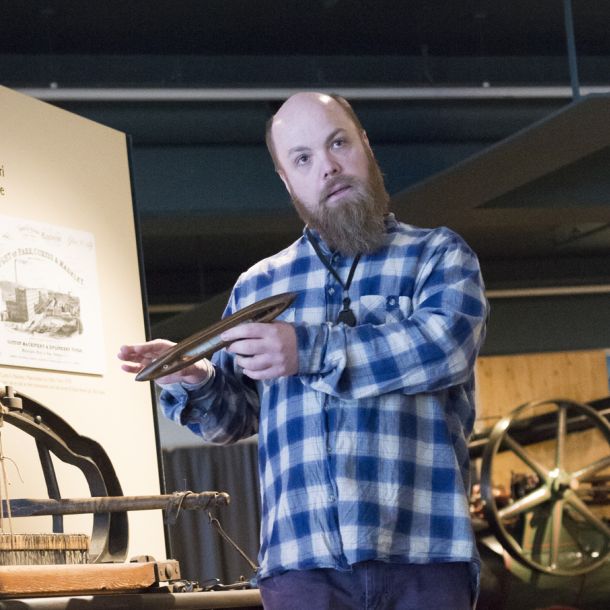 Man holding the shuttle of a mechanical loom on display. Photo