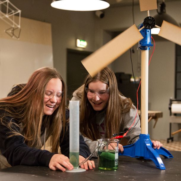 Two cheerful girls active around a windmill, a measuring cup and a beaker. Photo