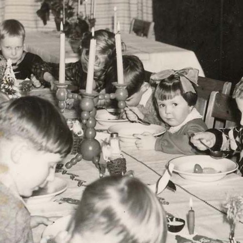 Image of several children sitting around a table eating. Photo.