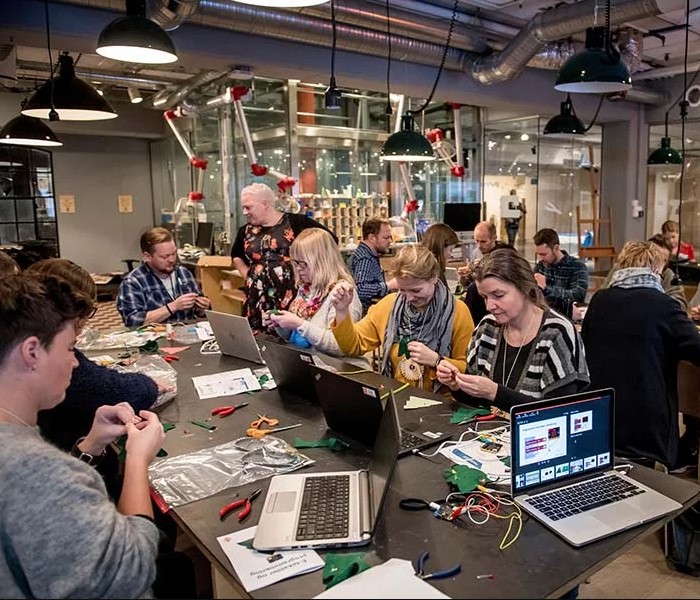 Fire voksne mennesker sitter ved et langbord med pc og notatblokker