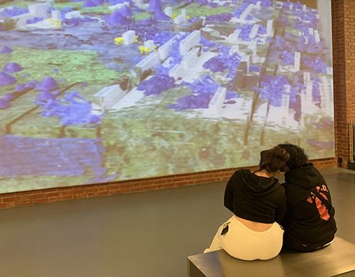 Two sit on a bench and look at the artwork