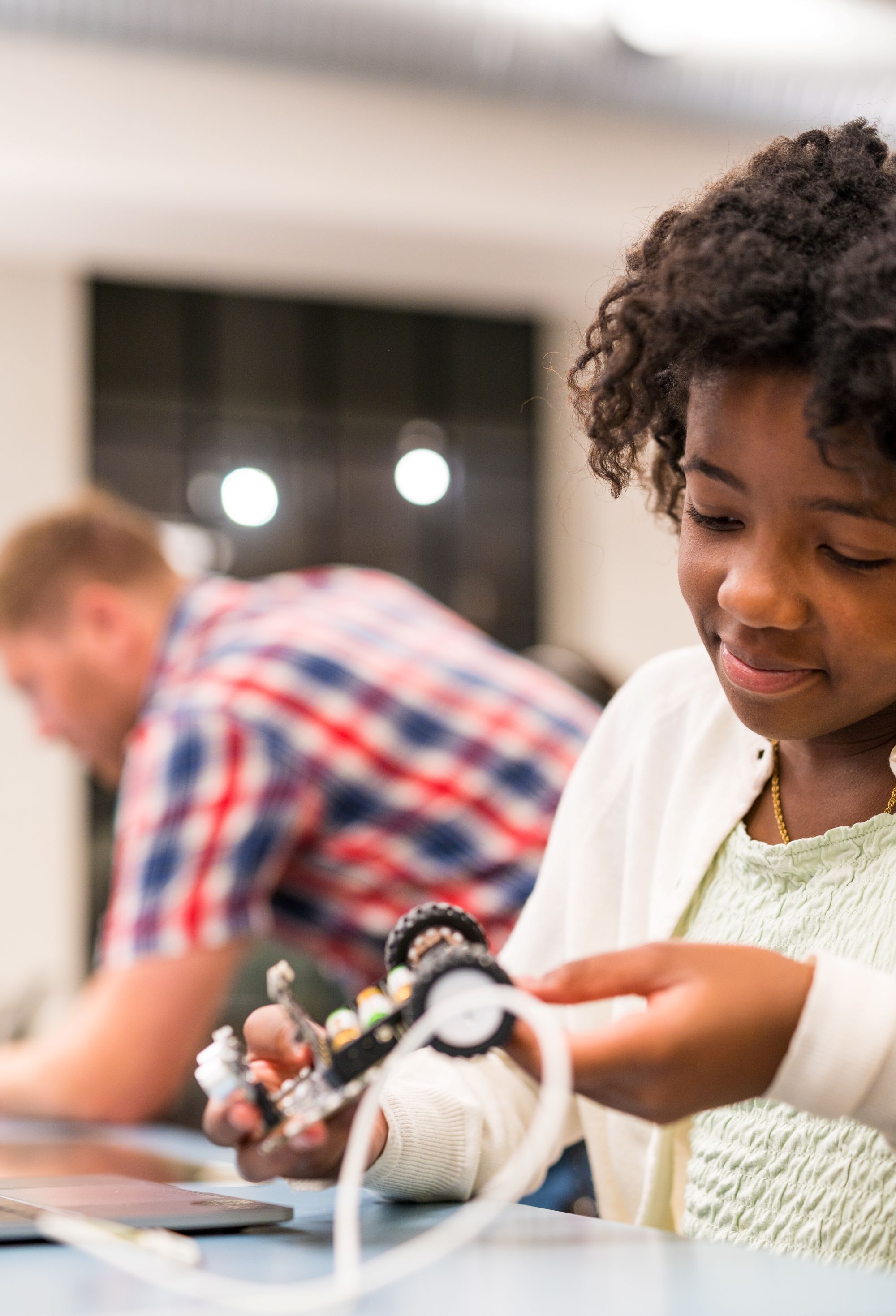 Jente og en vitensenterpedagog titter på en pc og  koder en bil, i et undervisningsrom