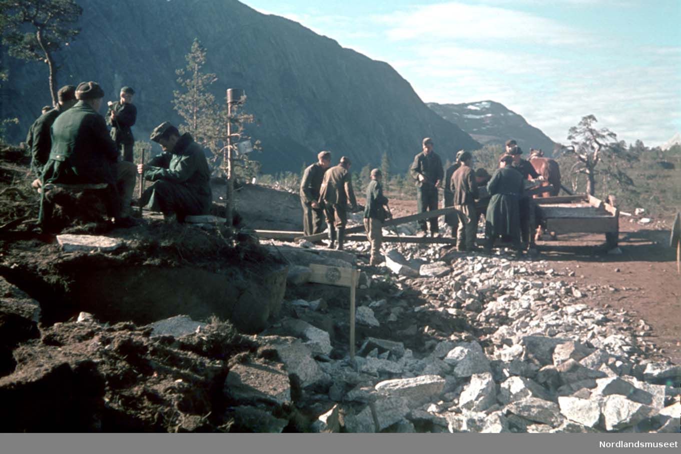Tvangsarbeidere rydder stein, militære sitter og ser på. Foto.