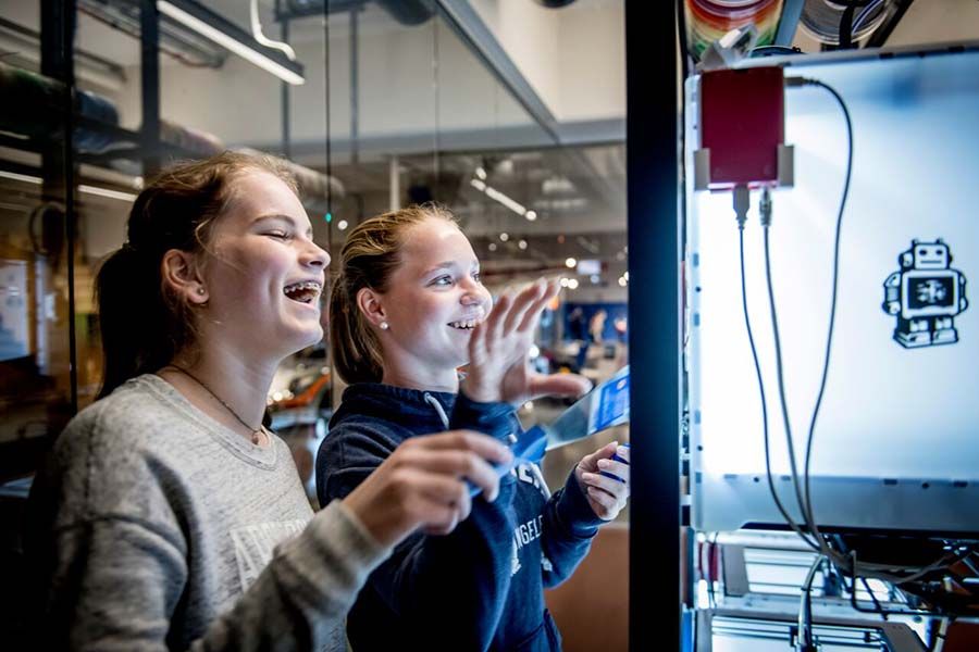 To jenter står ved en 3D printer og ler. Foto.