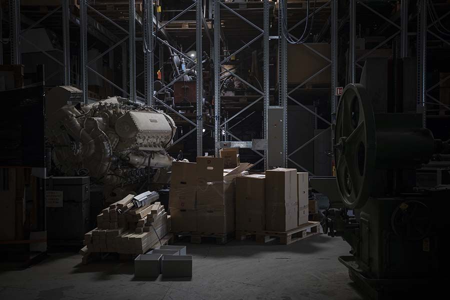 Et lager fylt med esker, planker og en stor forbrenningsmotor. Foto.