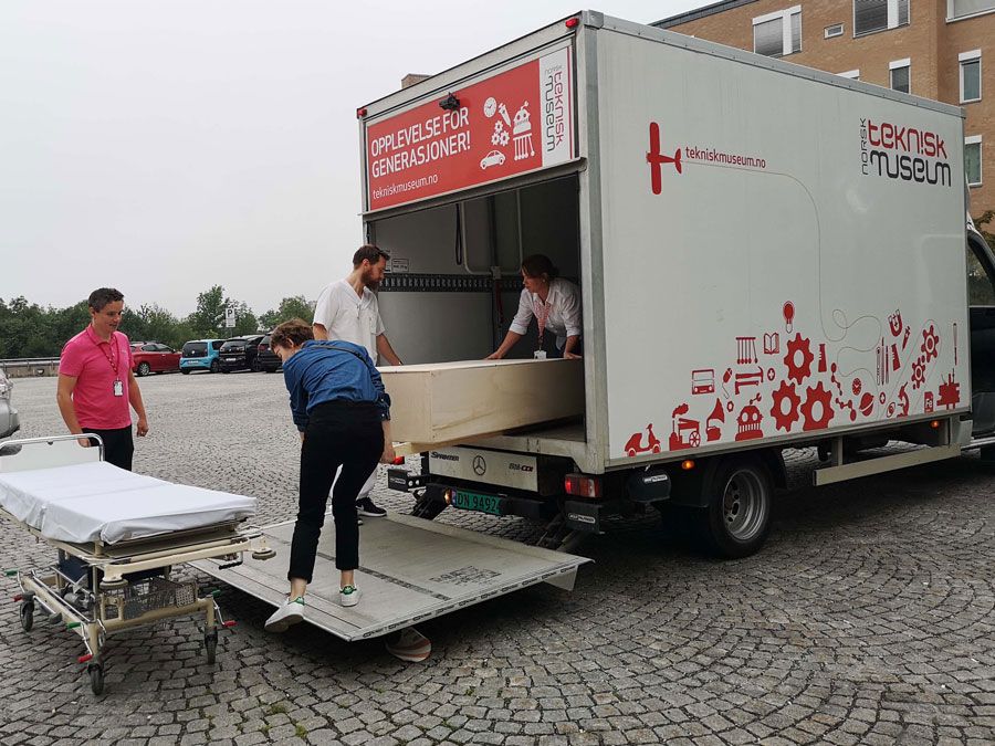 To menn og to kvinner laster en likkiste opp på en båre foran et sykehus.