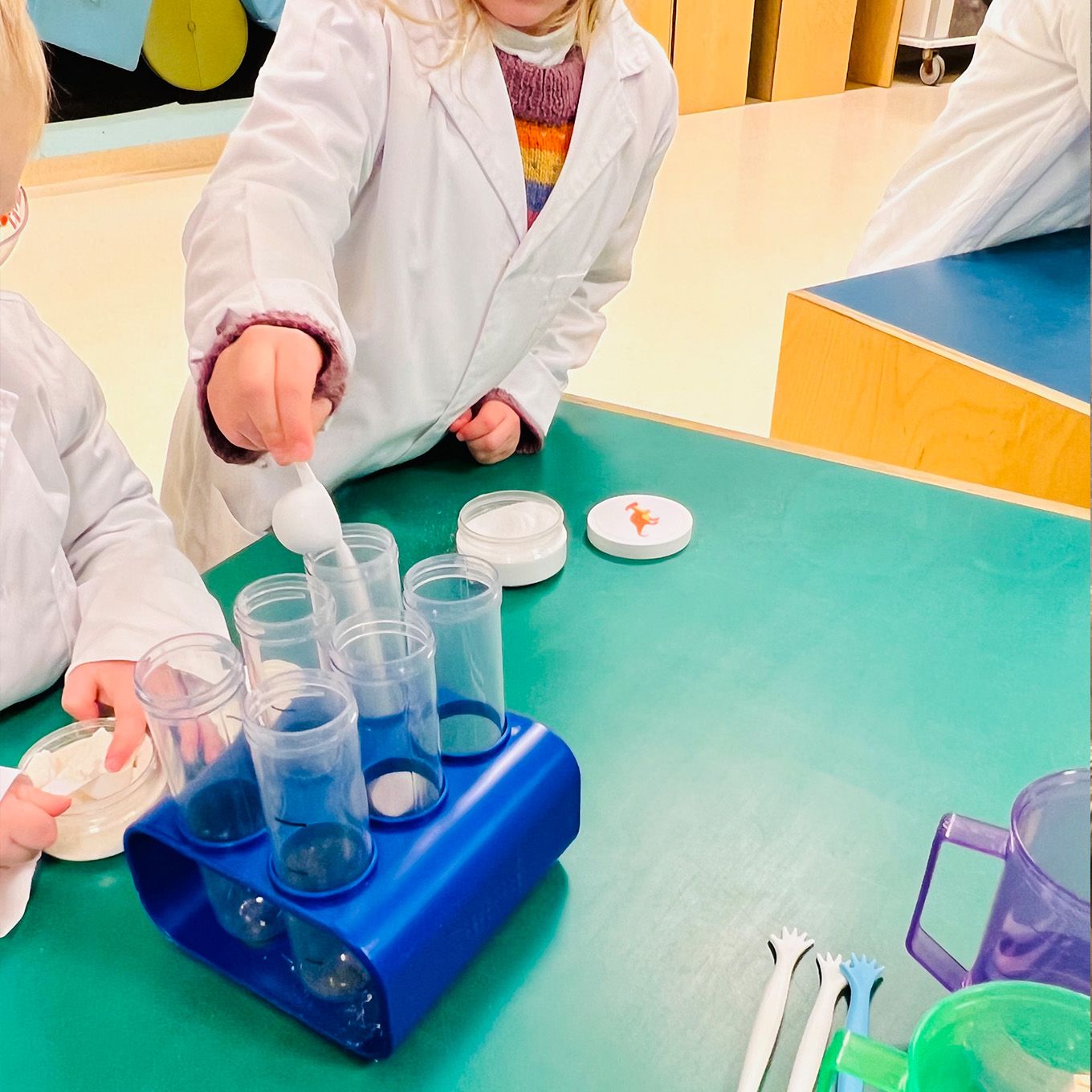 En barn i labfrakk som heller hvit pulver i enn jumbo testerør. Foto. 