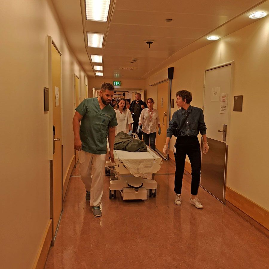Flere mennesker triller at tildekket lik gjennom en gang på et sykehus.