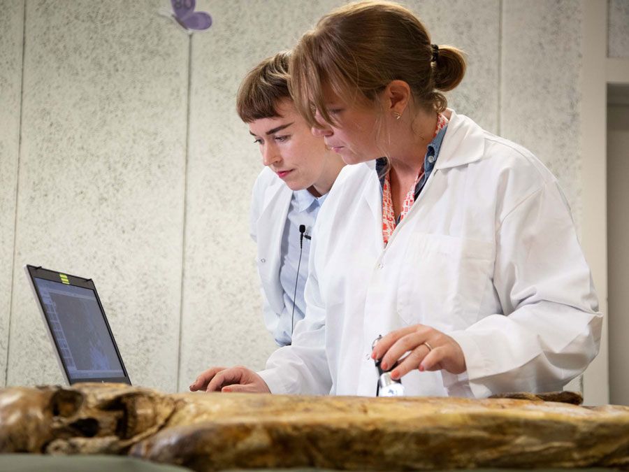 To kvinner med labfrakk tar prøver av et gammelt kolera lik.