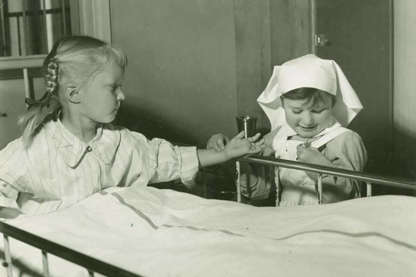 To jenter leker pasient og sykepleier. Historisk foto.