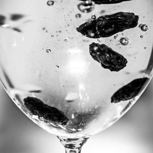 Rosiner i et vinglass med karbonisert vann. Foto