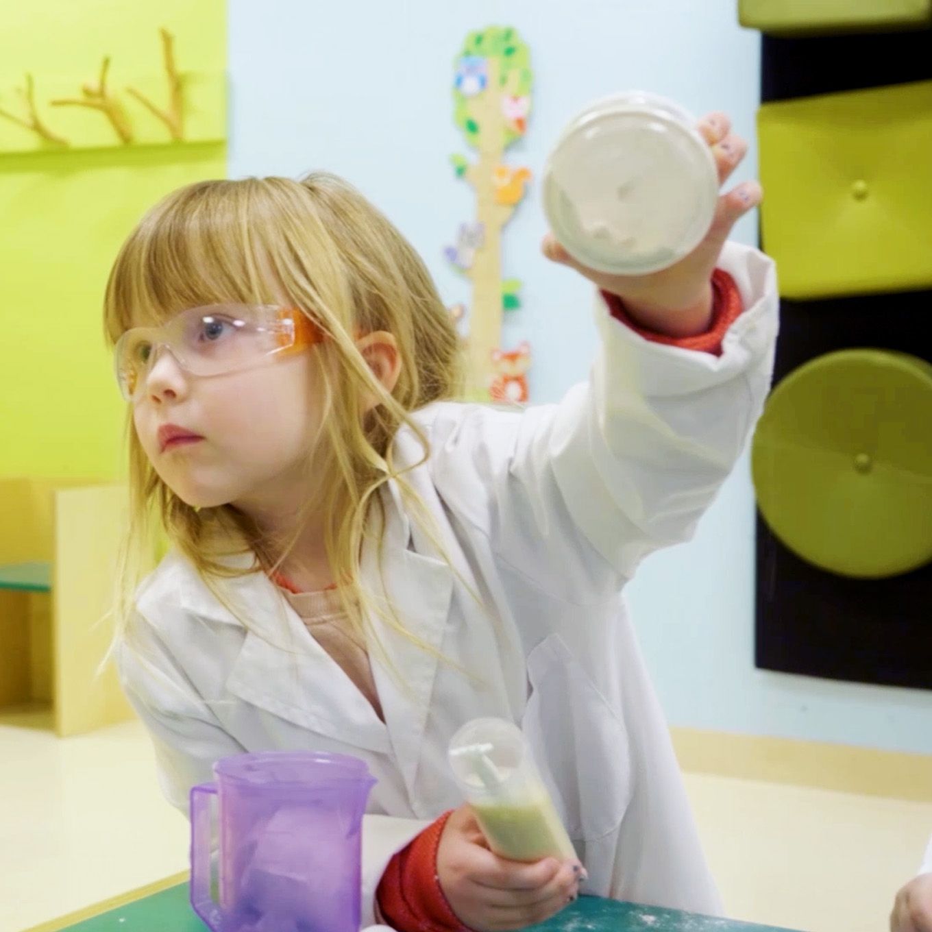 En jente i labfrakk rekker opp hånden. Foto. 