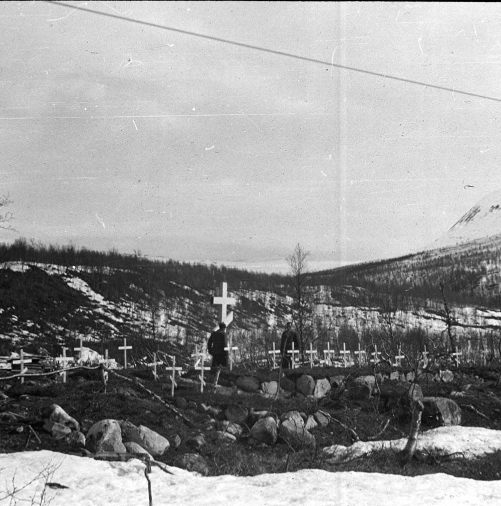To tvangsarbeidere på en gravplass med mange enkle trekors. Foto