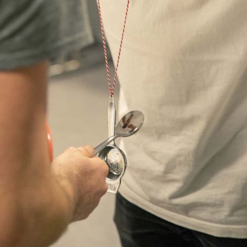 En gutt slår en skje mot en annen skje som er festet i en snor. Foto