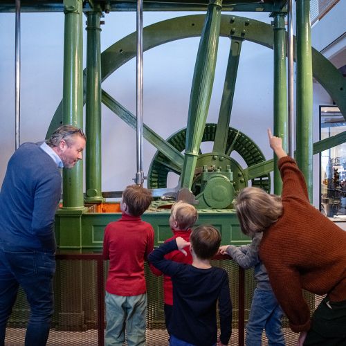 En familie med to voksne og barn som ser på en grønn dampmaskin